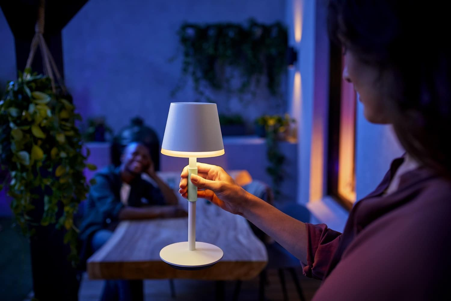 A woman holds a white and green lamp outdoors with a person in the background.