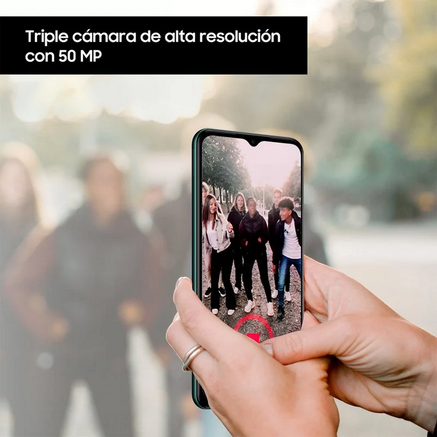 Una persona sostiene un teléfono que muestra un video de personas caminando. Texto arriba: Cámara triple con 50 MP.
