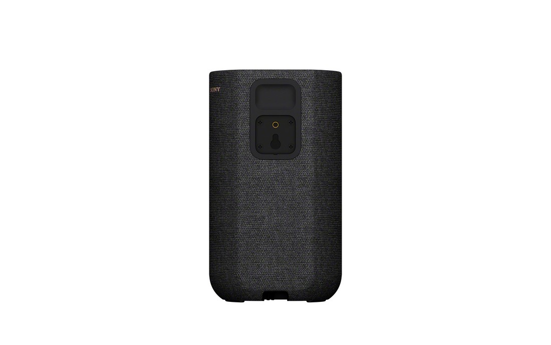 Un altavoz negro con textura de tela sobre un fondo blanco, la parte trasera muestra puertos de conexión.