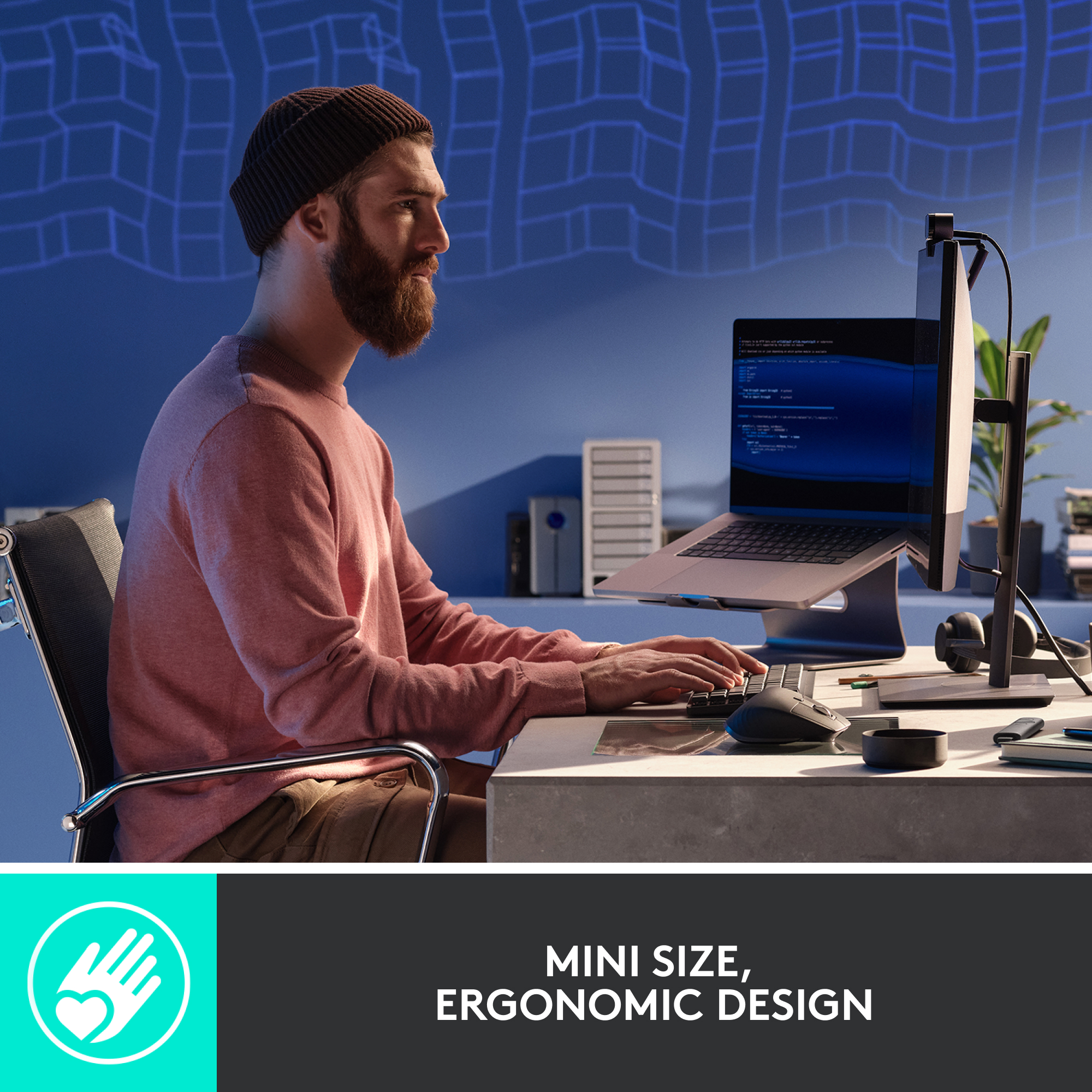 Homme avec une barbe travaillant sur un ordinateur portable, avec un écran de bureau et un clavier.