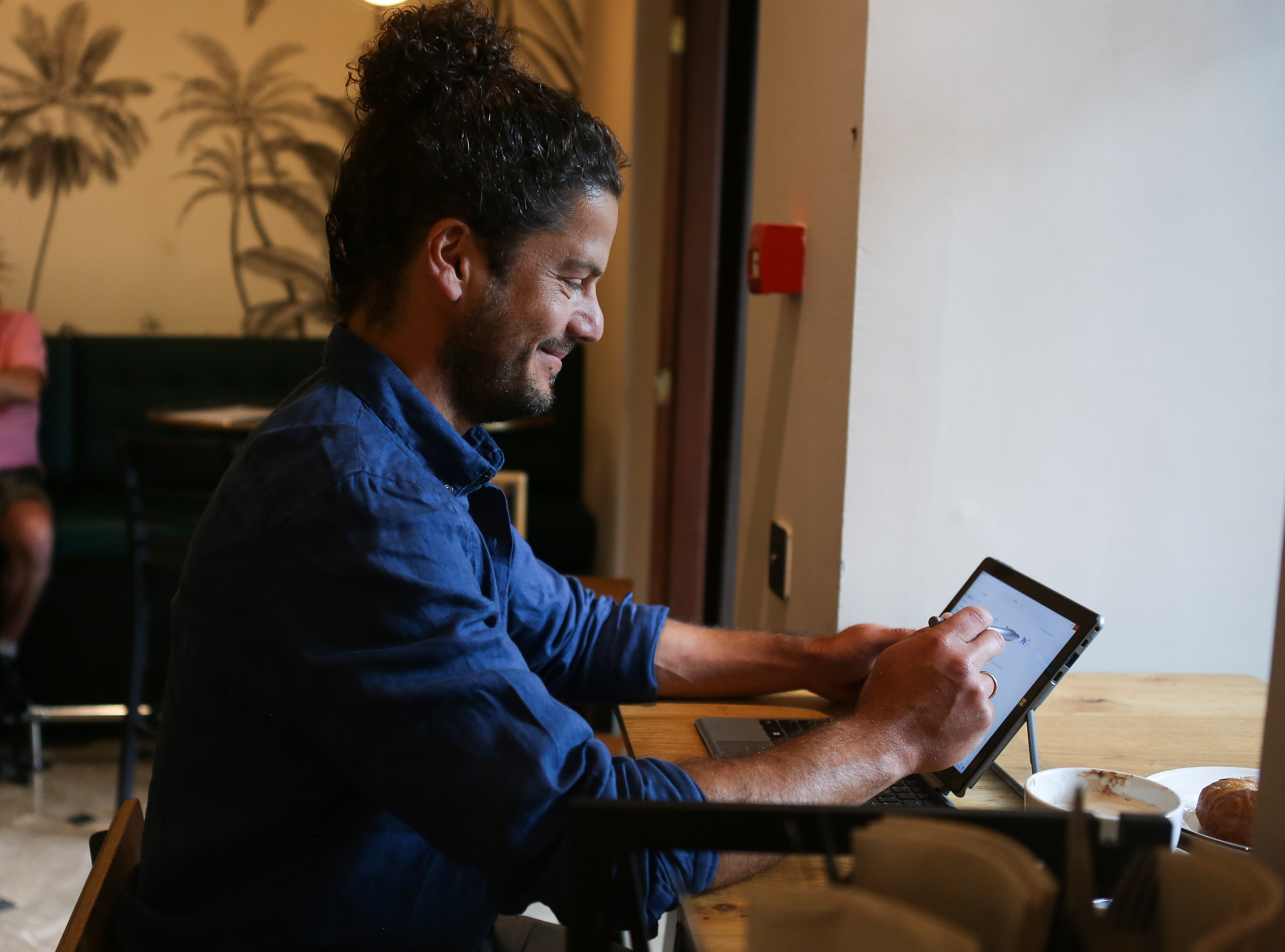 Ein Mann mit lockigem Haar, der in einem Café ein Tablet mit Stift benutzt.