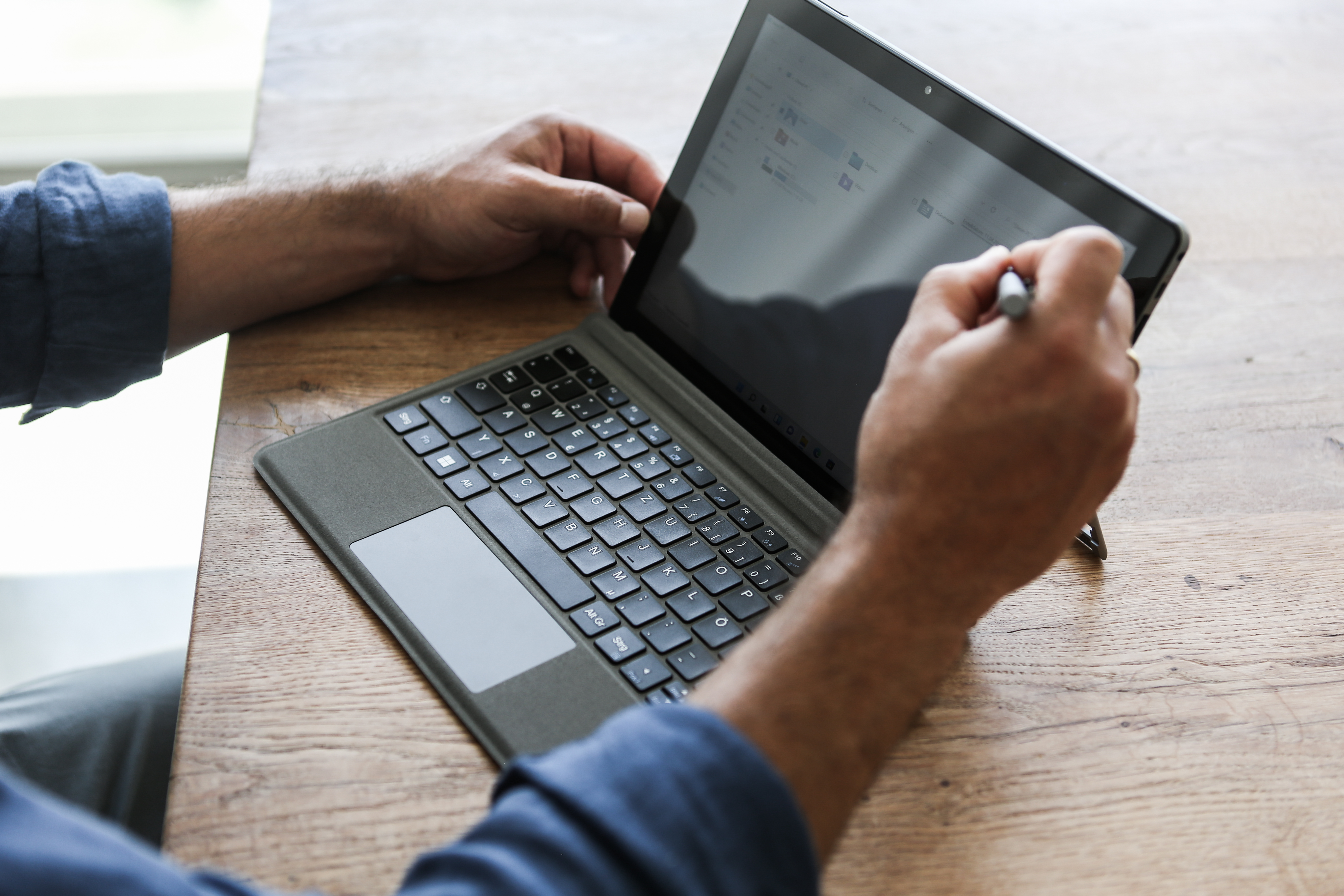 Eine Person benutzt ein Tablet mit Tastatur und schreibt mit einem Stift auf dem Bildschirm.
