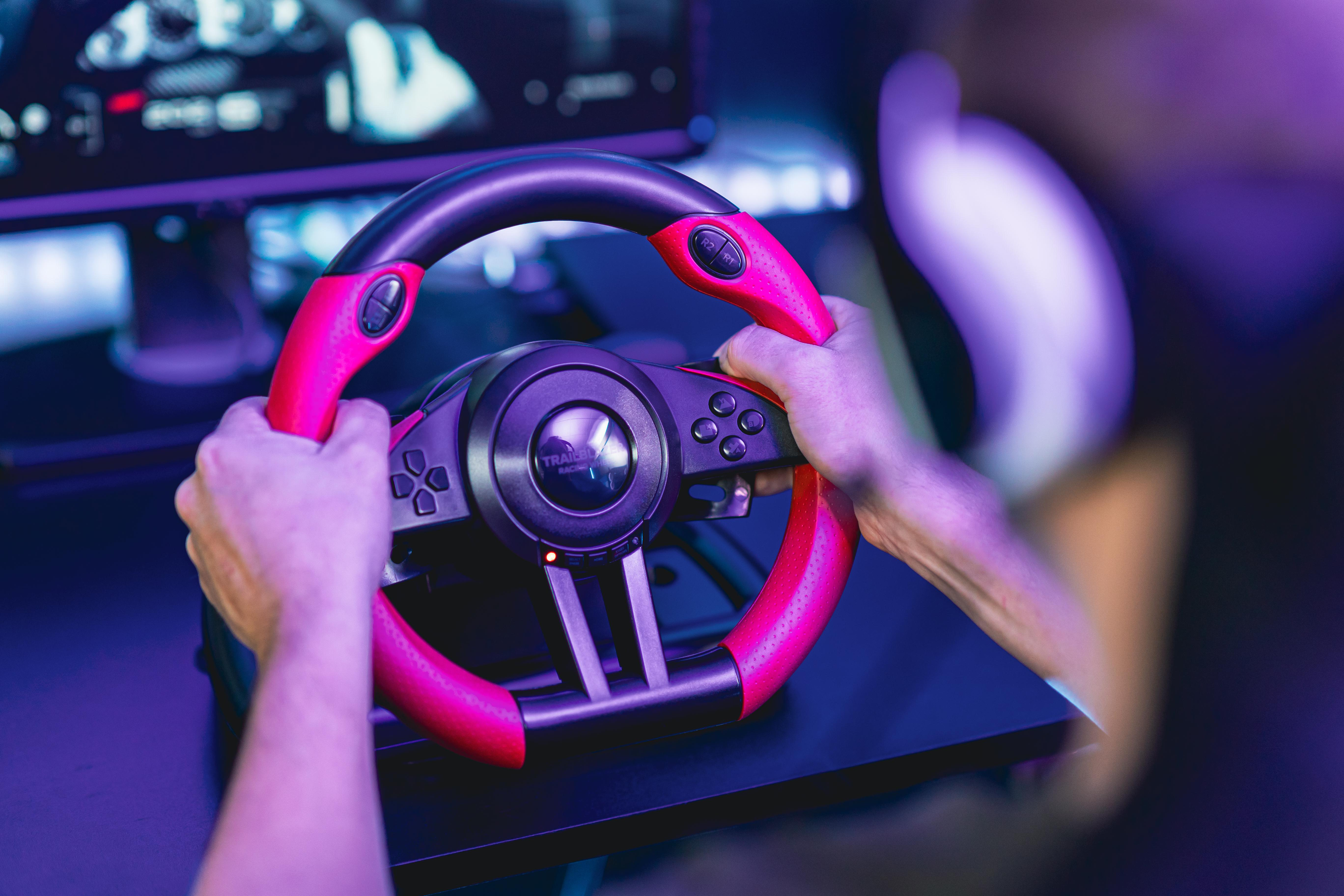 Hände halten ein rotes und schwarzes Gaming-Lenkrad mit Knöpfen, vor einem Hintergrund.