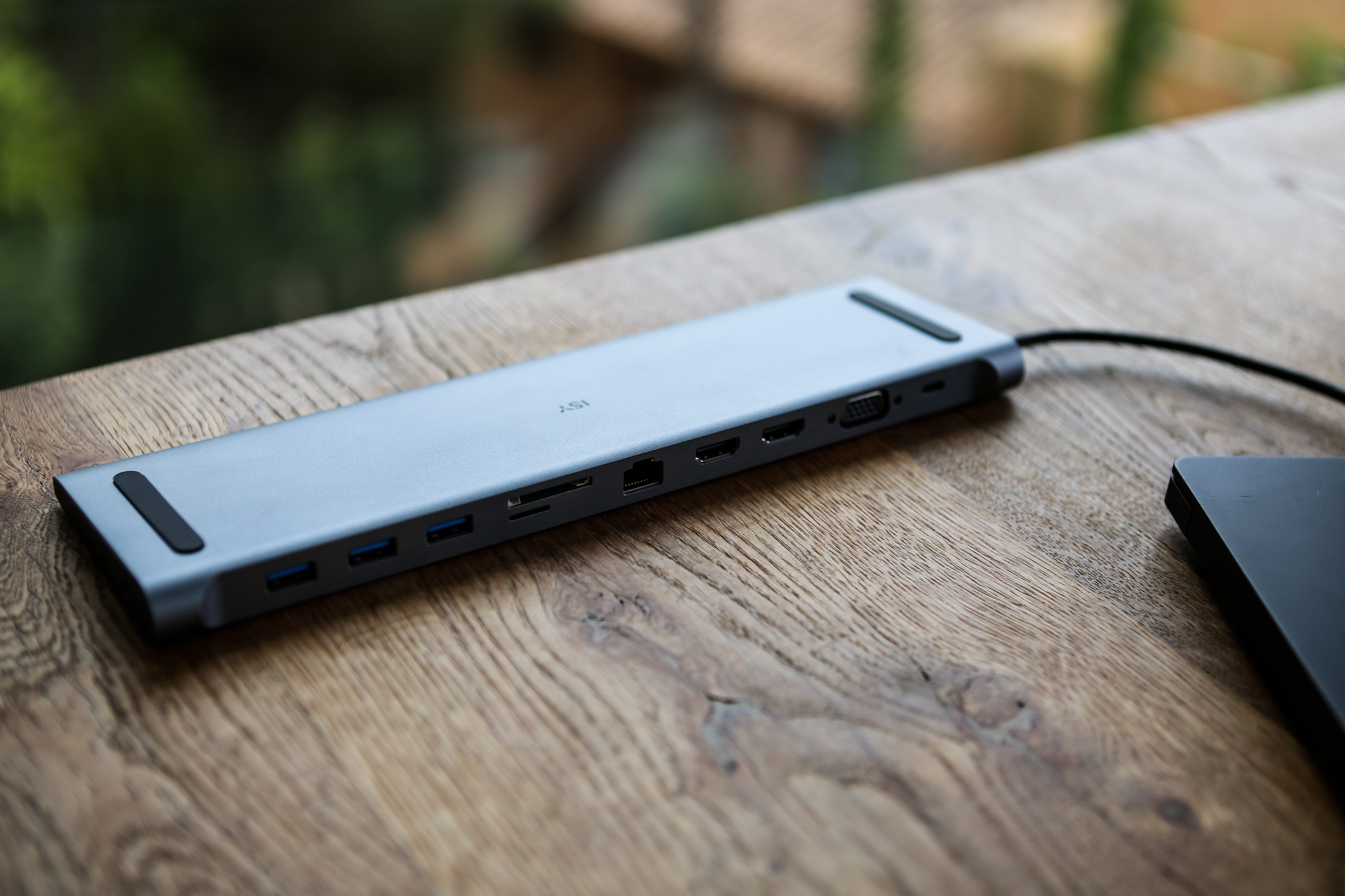 Ein grauer USB-C-Hub auf einem Holztisch mit einem Laptop im Hintergrund.