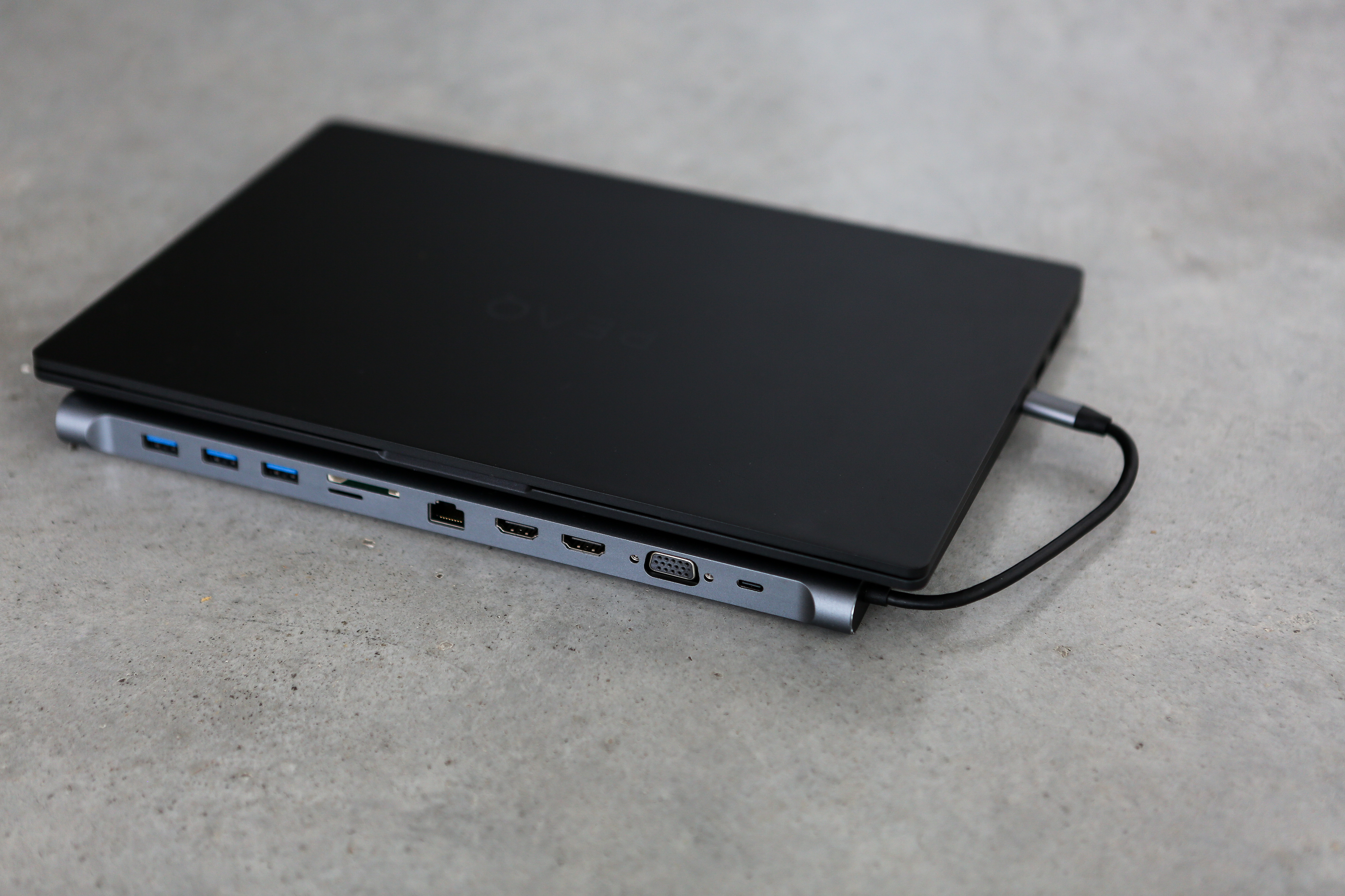 Laptop auf einem silbernen Hub mit Anschlüssen. Ein Ladekabel ist angeschlossen.