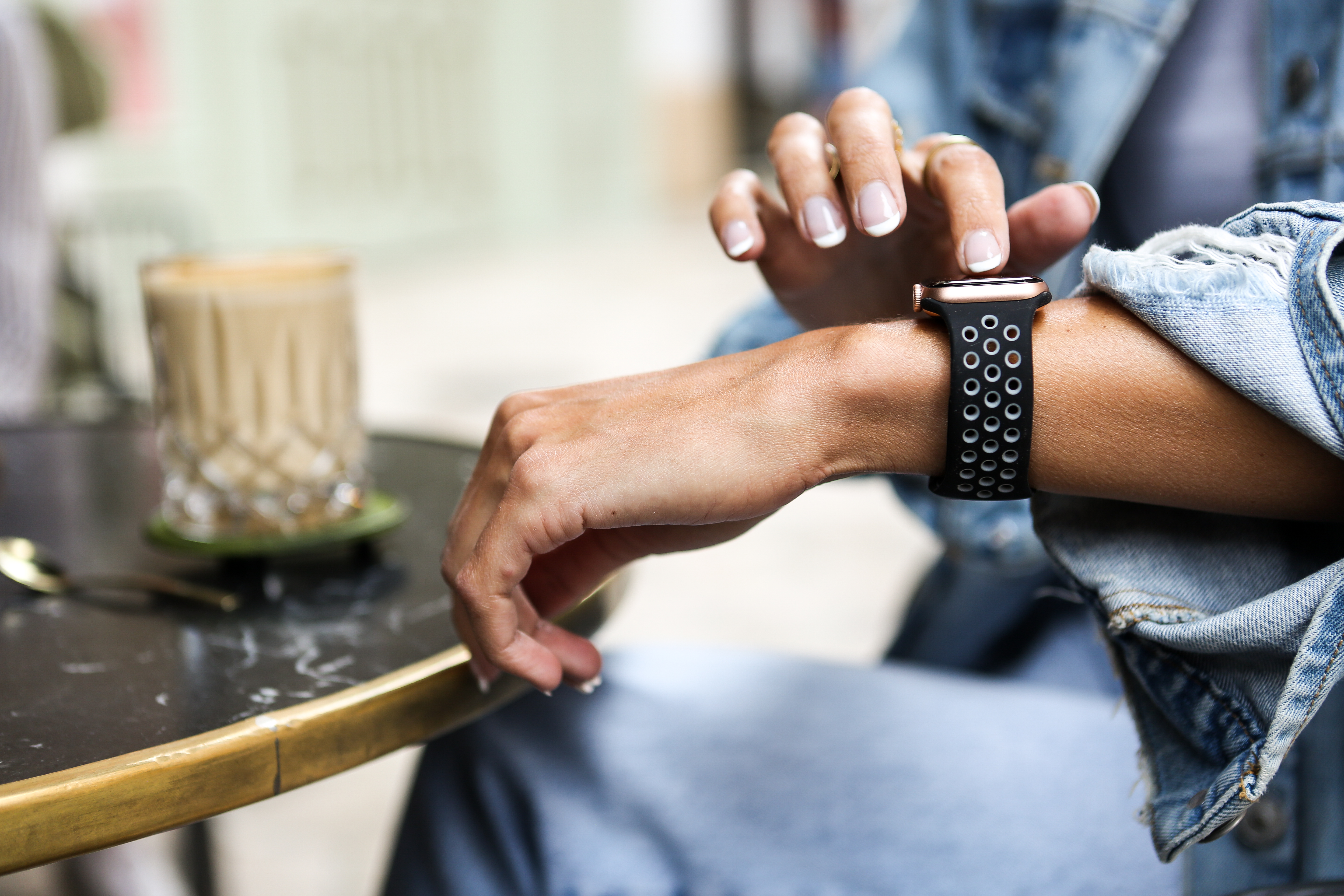 Person trägt Apple Watch mit schwarzem Sportarmband, überprüft die Zeit. Kaffee und Tisch sichtbar.