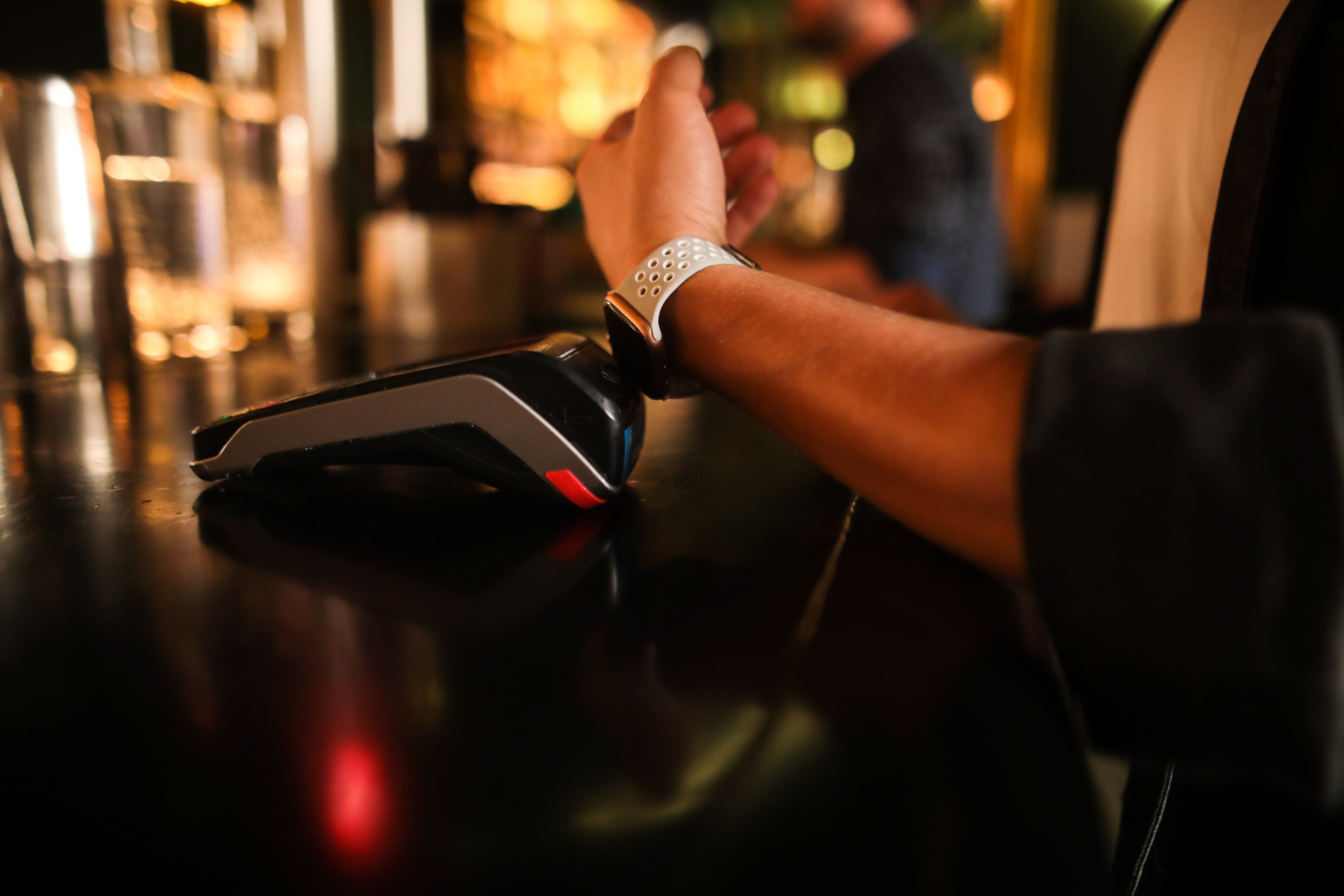 Person benutzt Smartwatch zum Bezahlen an einer Bar, auf schwarzer Oberfläche.