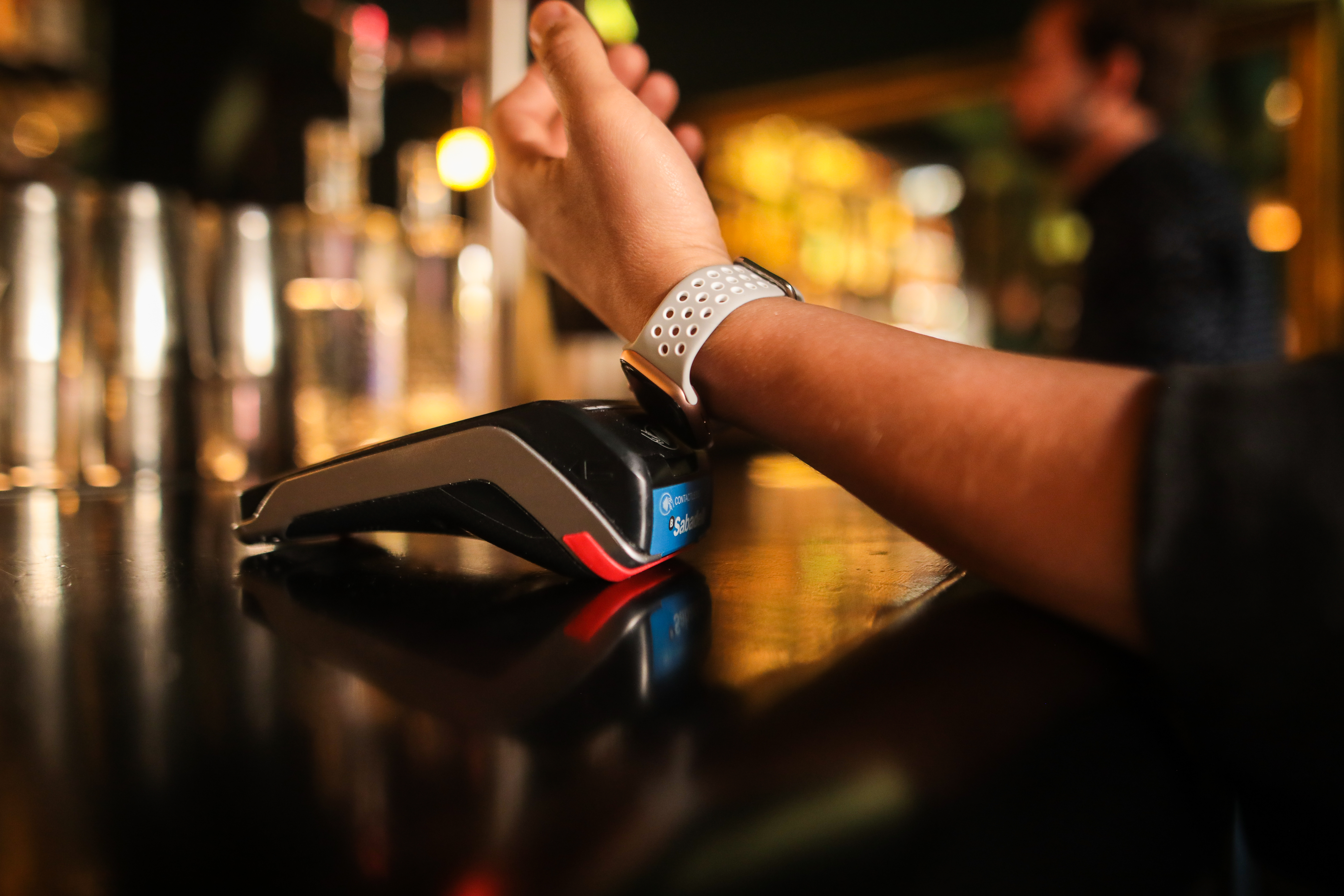 Person trägt Smartwatch, bezahlt an einer Bar mit kontaktlosem Bezahlen.