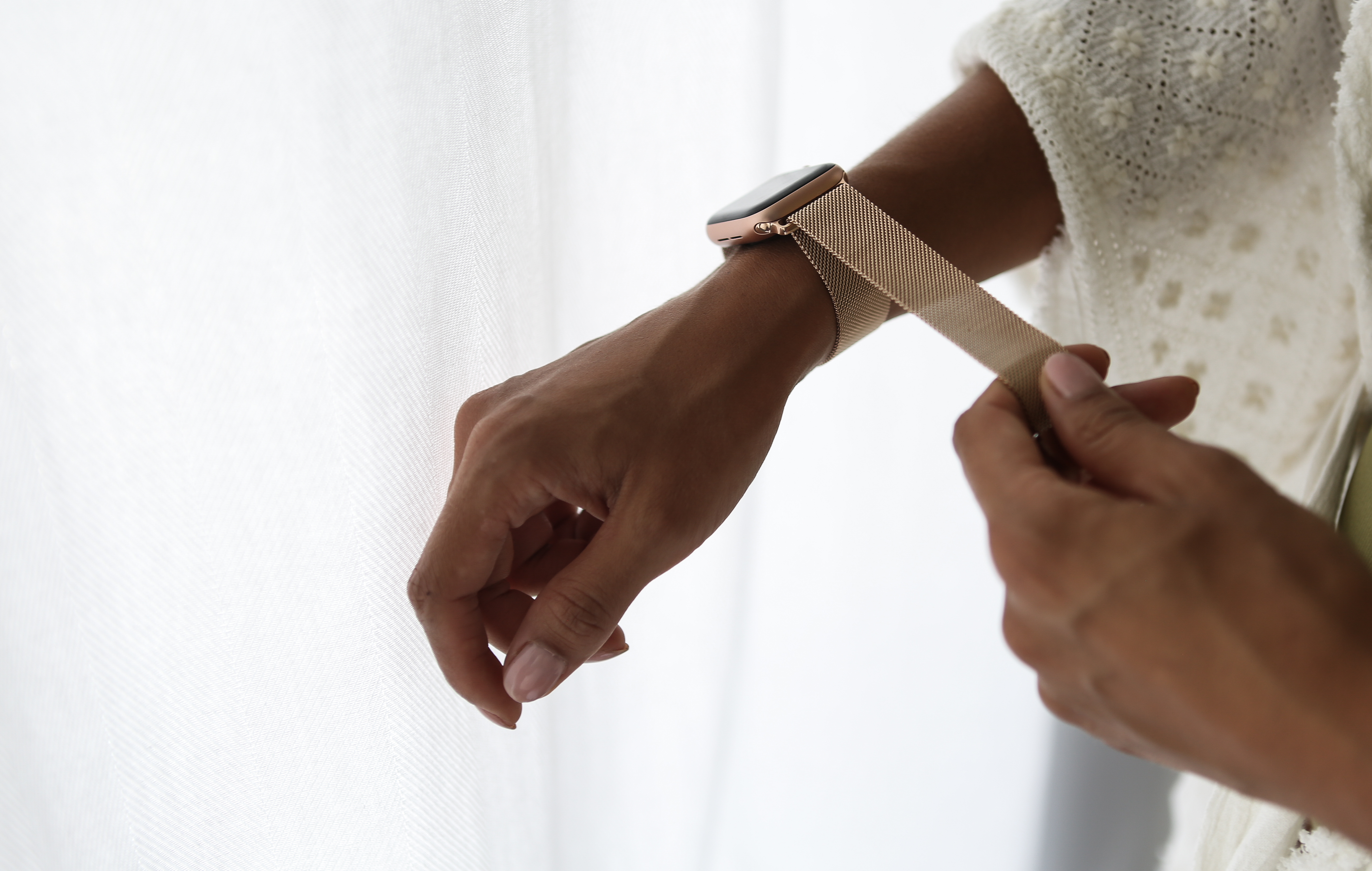 Person passt ein goldenes Mesh-Armband an ihr Handgelenk an, in der Nähe eines weißen Vorhangs.