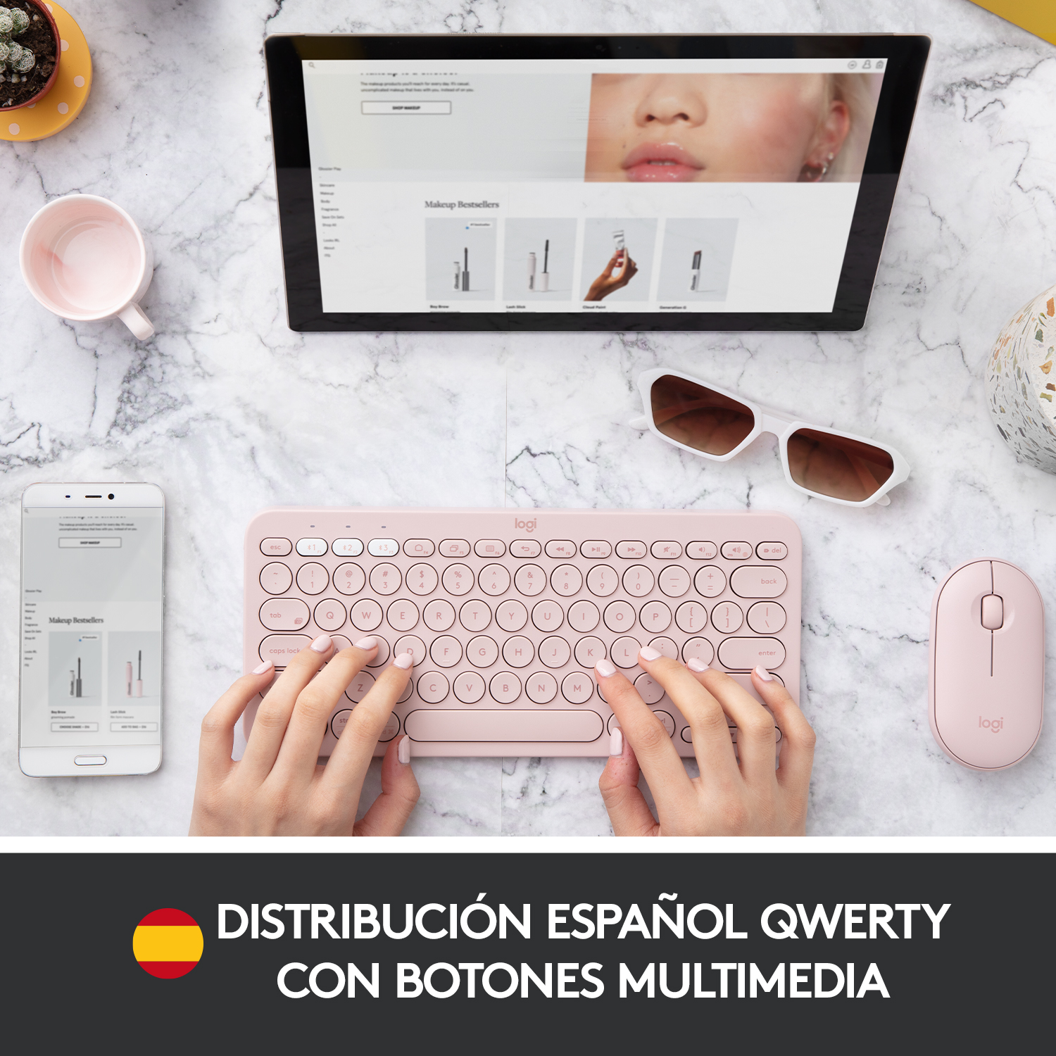 Teclado, ratón, tableta y teléfono rosas sobre superficie de mármol. Incluye texto en español.