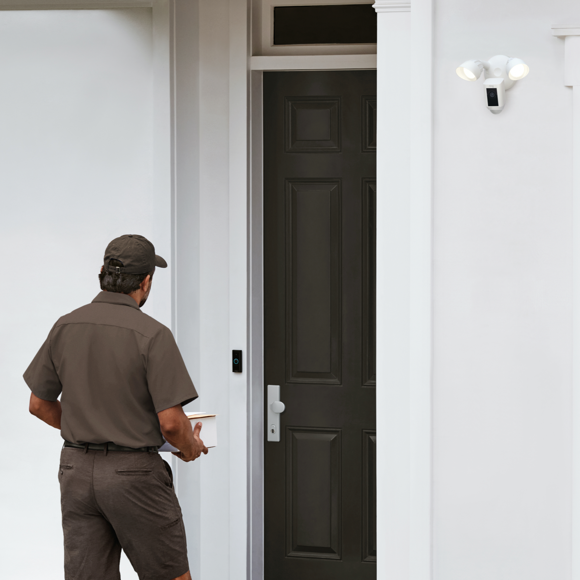 Delivery man in uniform, holding a package, approaching a door. White wall, door, and light.