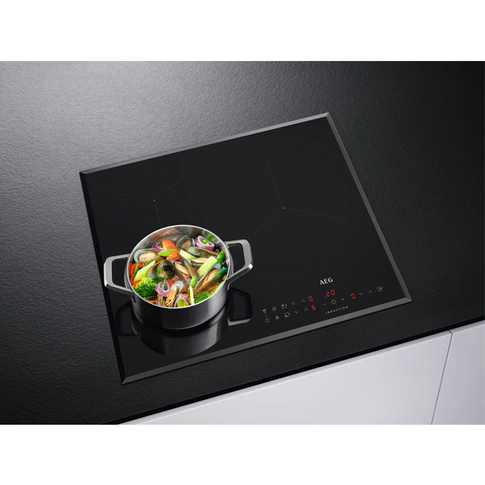 Placa de inducción negra con una olla de comida encima.