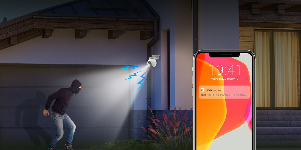 Scène de nuit : un cambrioleur s'approche d'une maison. Le téléphone affiche une notification de détection de mouvement.