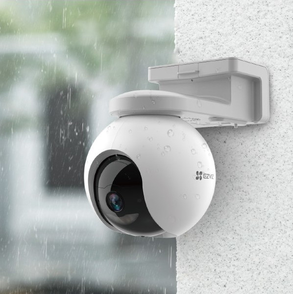 Caméra de sécurité EZVIZ blanche, montée sur un mur. Gouttes de pluie visibles.