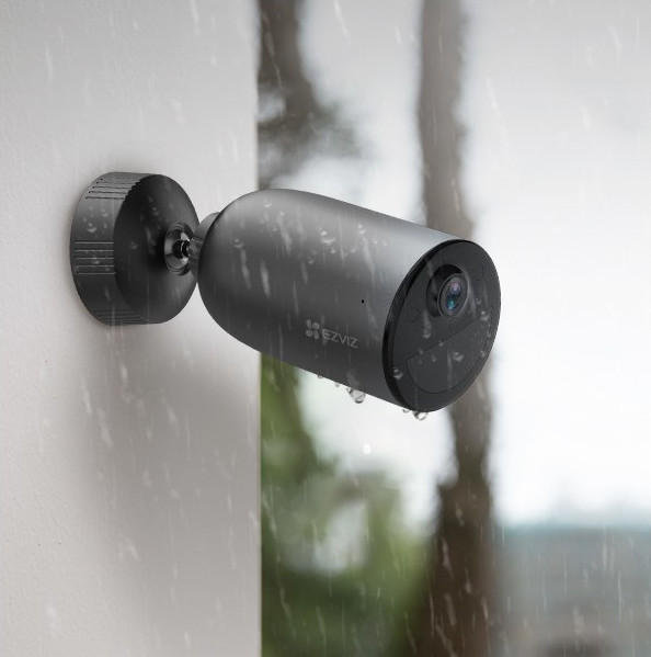 Black EZVIZ security camera mounted on a wall. It is raining, and water droplets are visible.