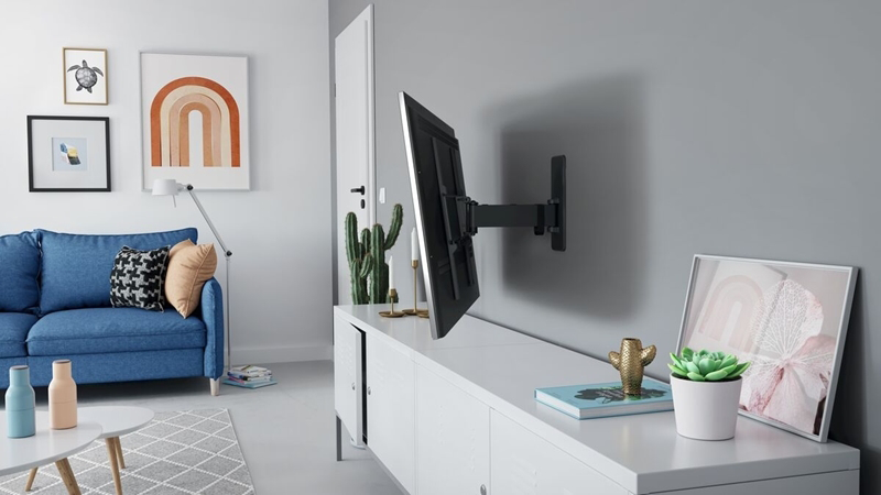 Nappali falra szerelt TV-vel, kanapéval, kaktuszokkal és keretezett művészettel. Fehér szekrény. Modern design.
