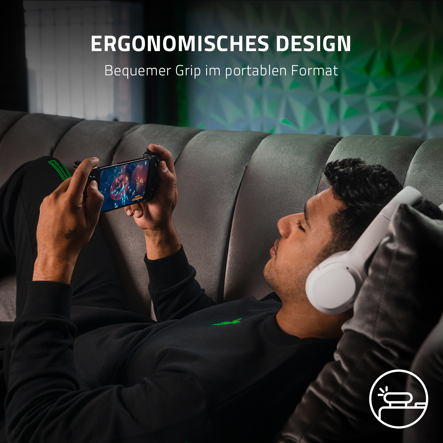 Mann auf dem Sofa, der ein Spiel auf dem Telefon mit einem Controller spielt. Er hat weiße Kopfhörer.