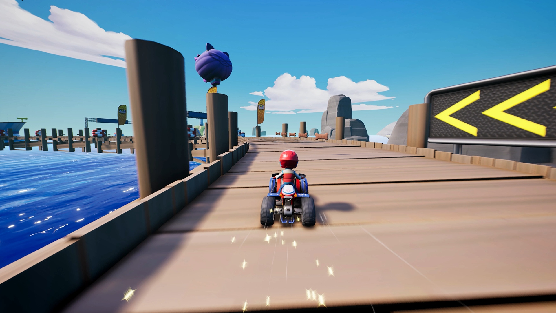 Ein Kart-Rennfahrer fährt auf einer Strecke in der Nähe von Wasser. Die Strecke ist aus Holz, der Himmel ist blau.