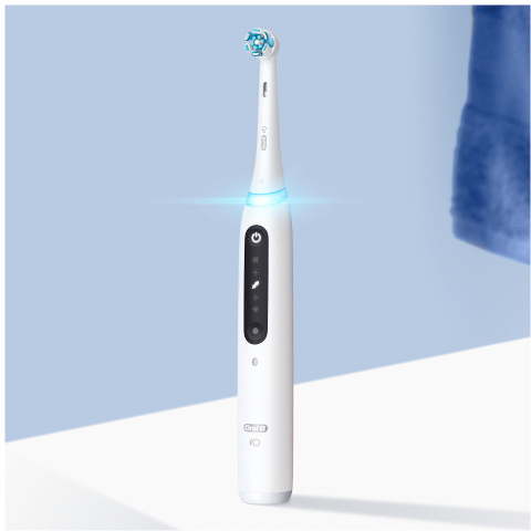 Une brosse à dents électrique Oral-B iO blanche avec une lumière bleue, sur fond bleu clair.