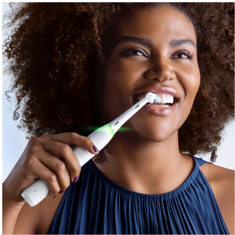 Une femme se brossant les dents avec une brosse à dents électrique, souriante. Fond bleu clair.