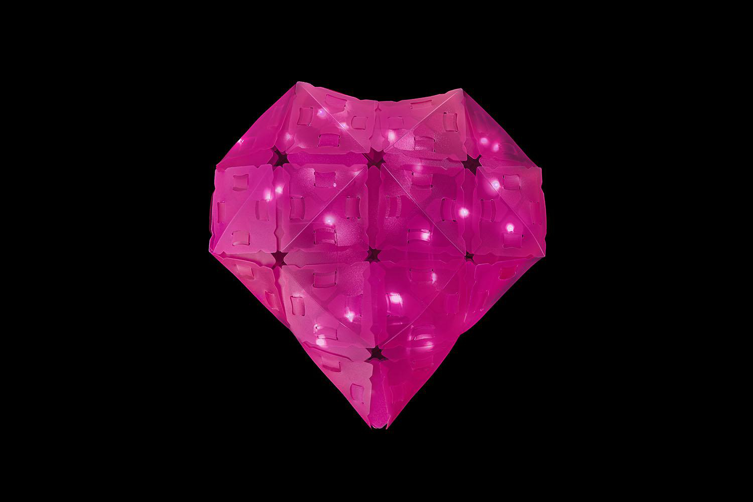 Rosa herzförmiges Objekt mit Lichtern, schwarzer Hintergrund, geometrisches Design.