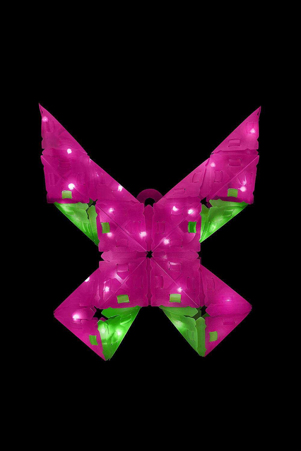 Eine rosa und grüne schmetterlingsförmige Leuchte vor schwarzem Hintergrund.