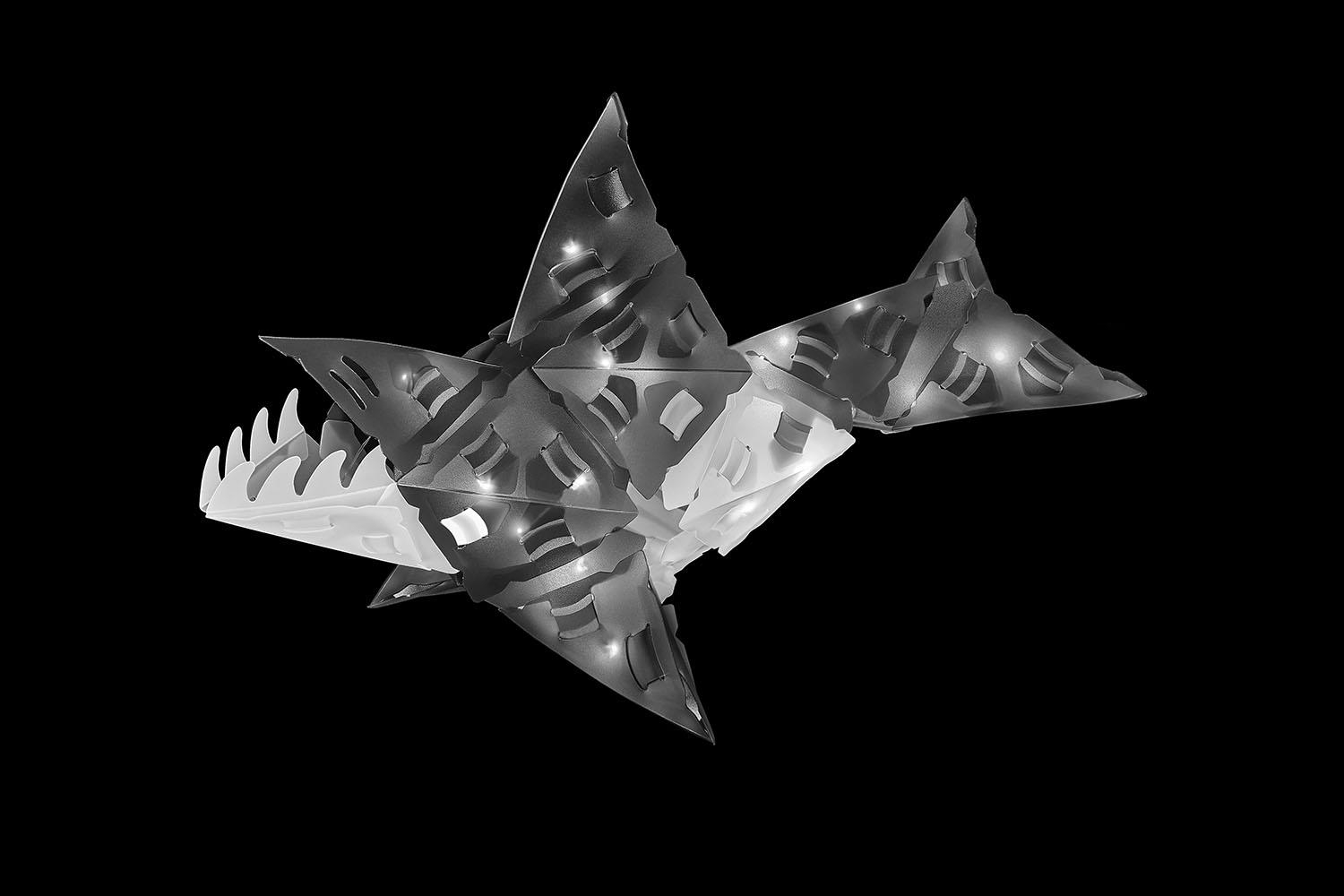 Ein Hai aus geometrischen Formen, beleuchtet und isoliert vor schwarzem Hintergrund.