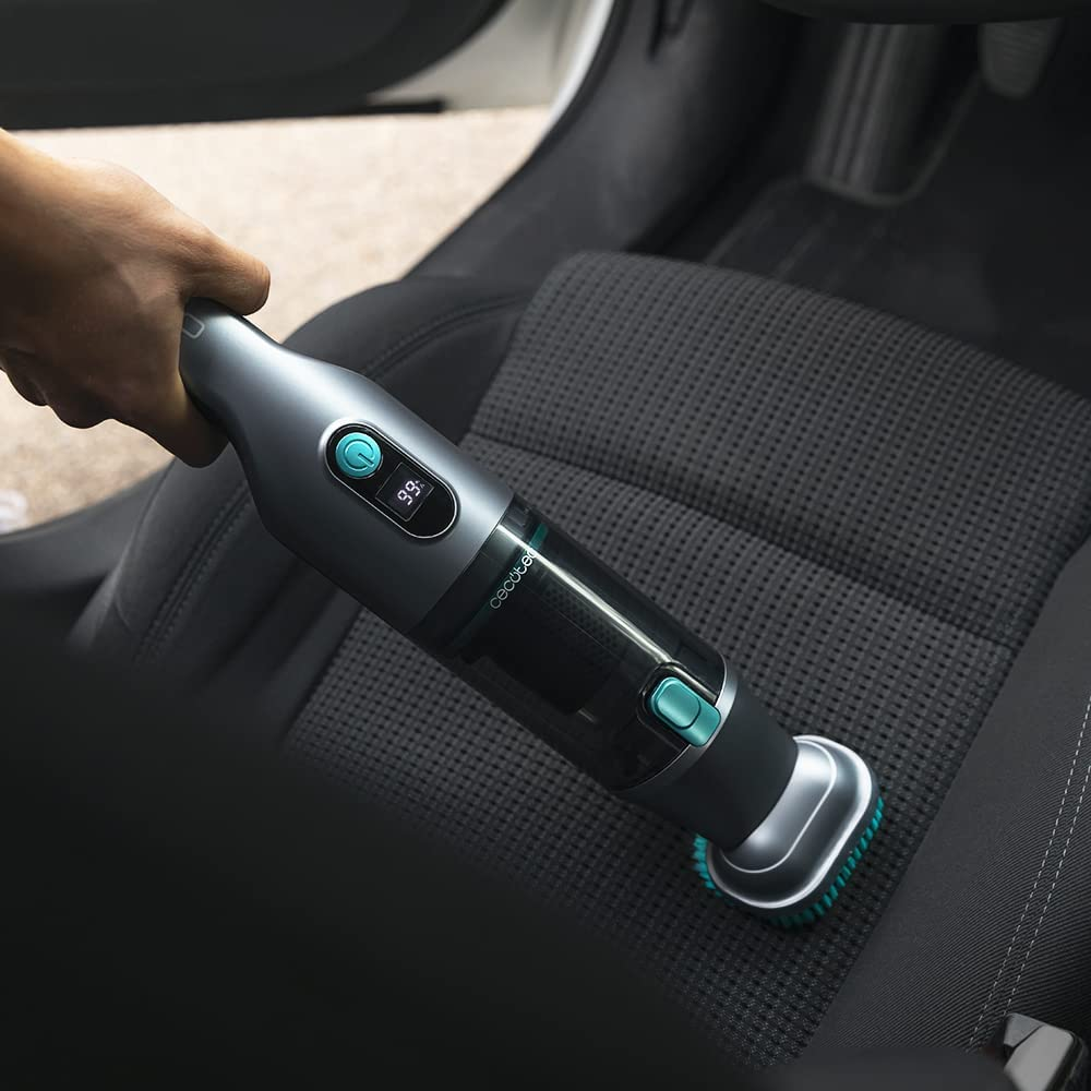 Una persona aspirando un asiento de coche con una aspiradora de mano. El asiento es negro.