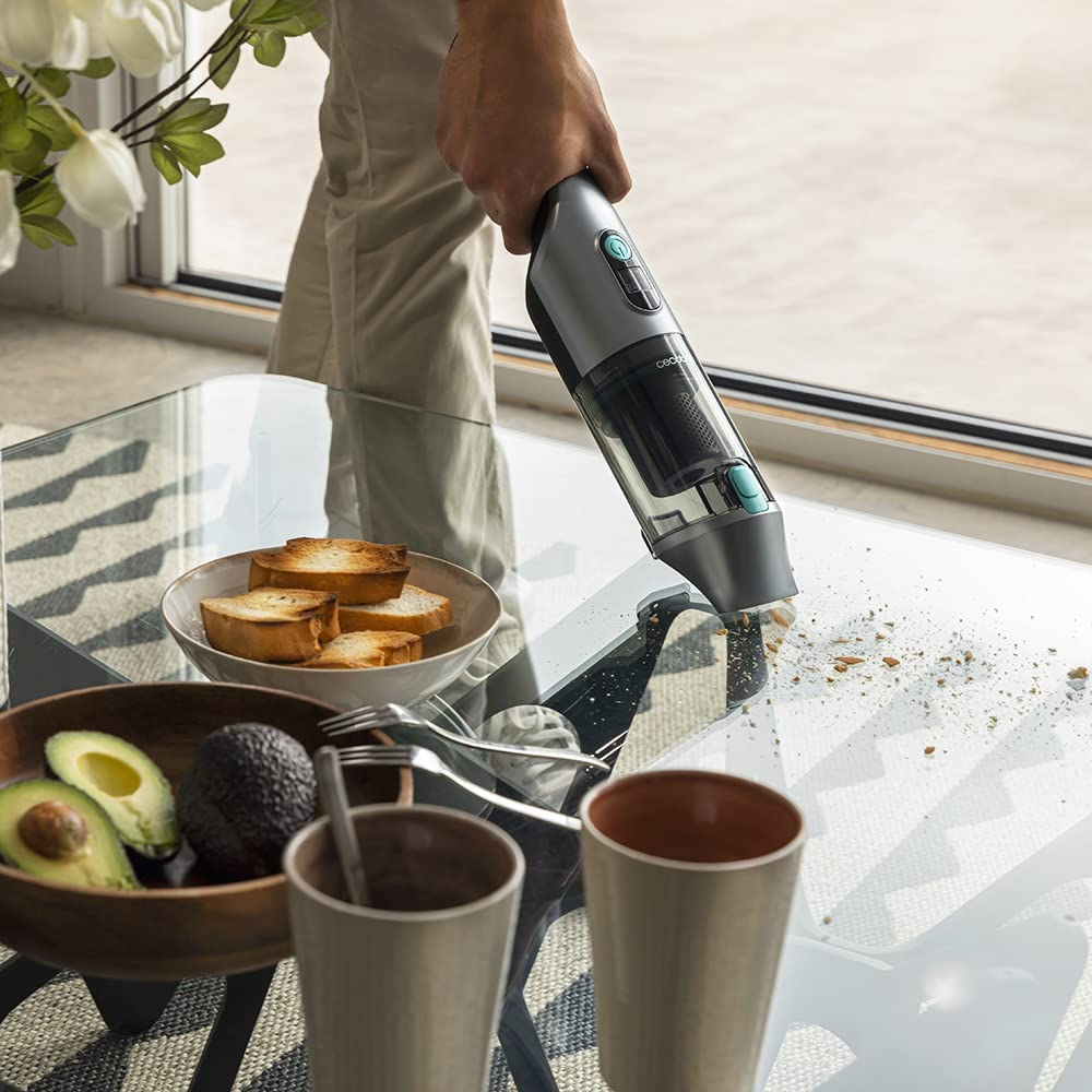 Una mano aspirando migas de una mesa de cristal, con comida y bebidas al frente.
