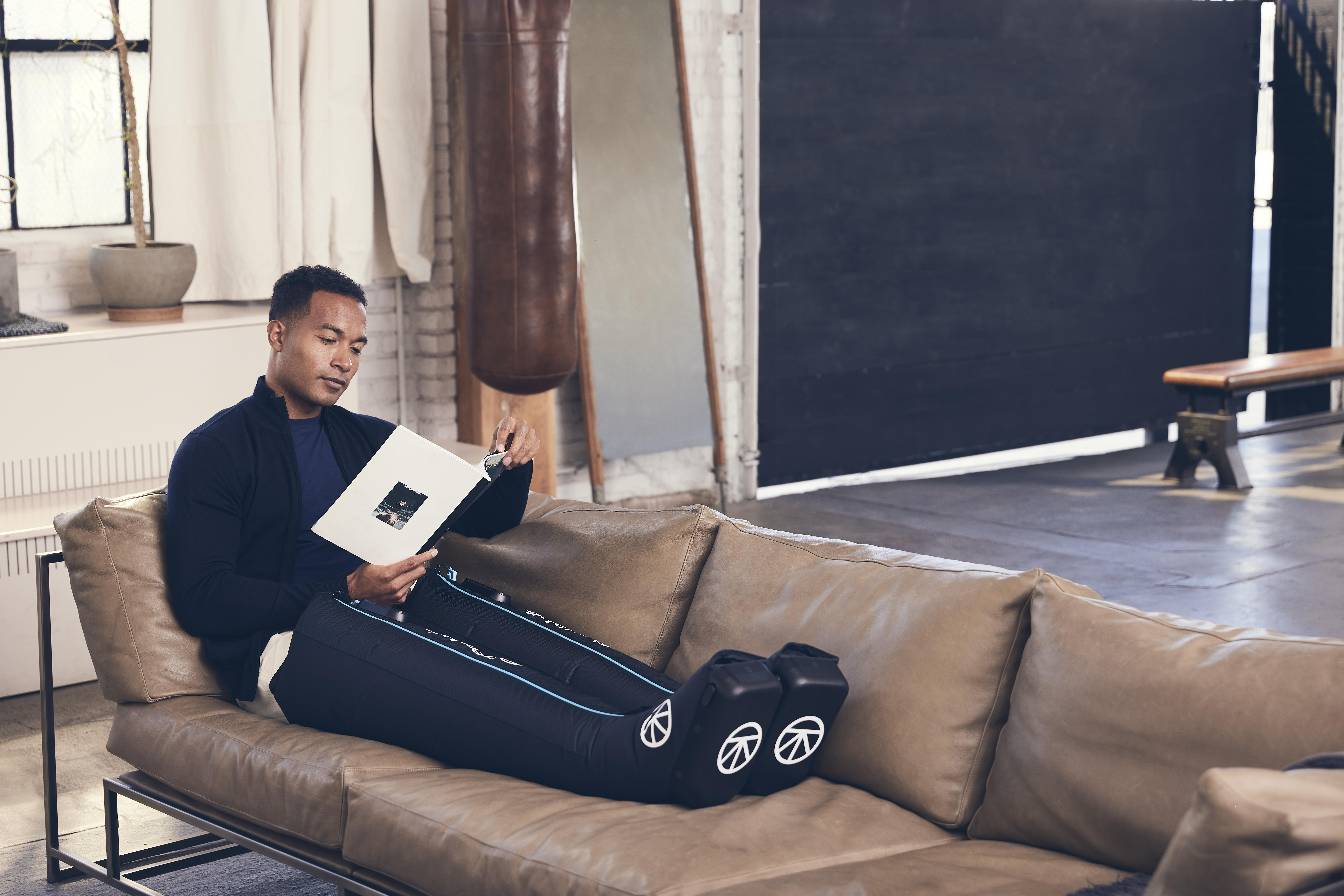 Ein Mann sitzt auf einer Couch und liest ein Buch, mit Bein-Erholungsgeräten.