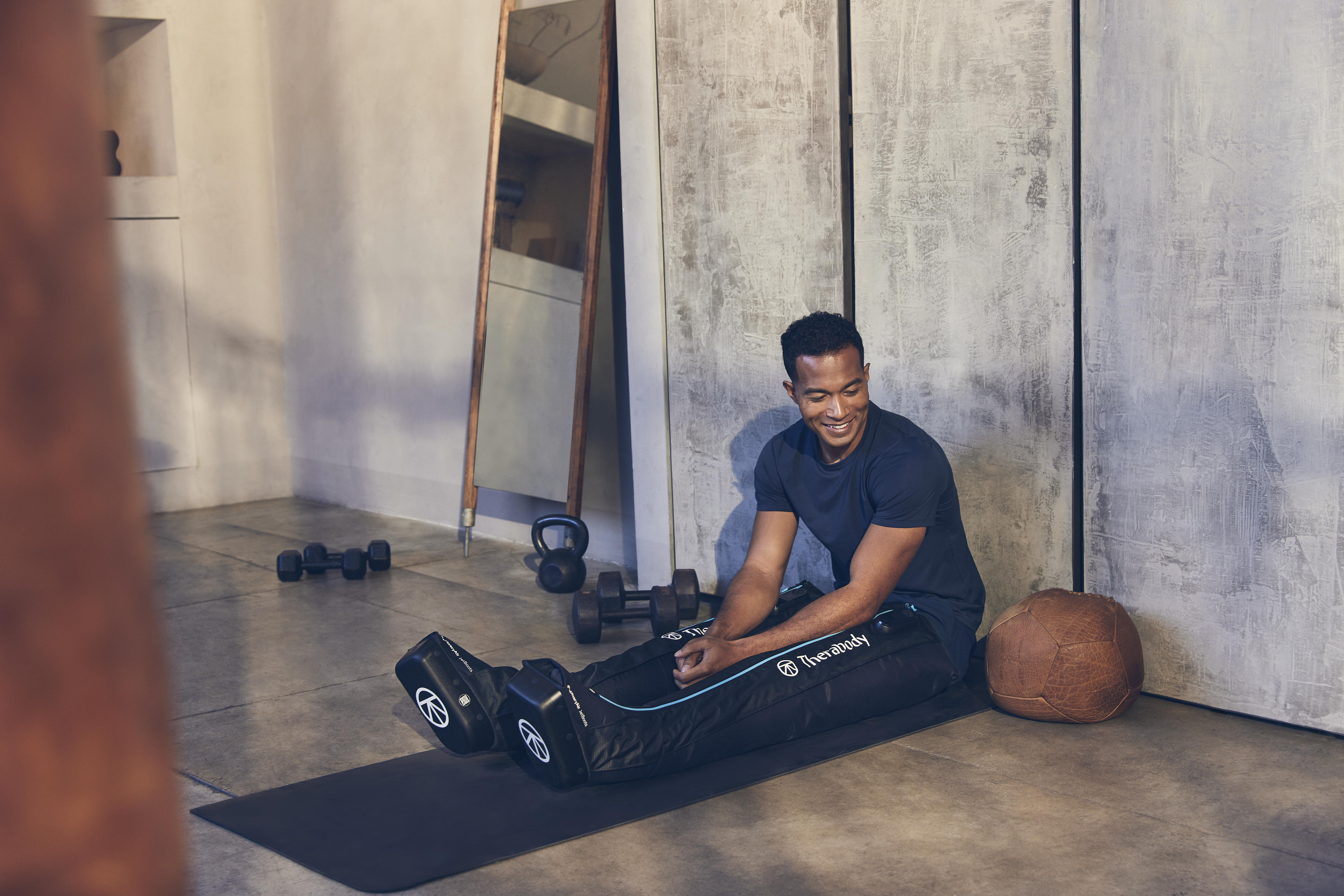 Mann in Kompressionsstiefeln, Fitnessstudio, lächelt, mit Trainingsgeräten.