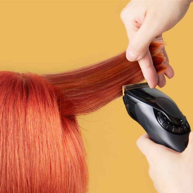 Hände schneiden rotes Haar mit einem Haarschneider. Gelber Hintergrund.