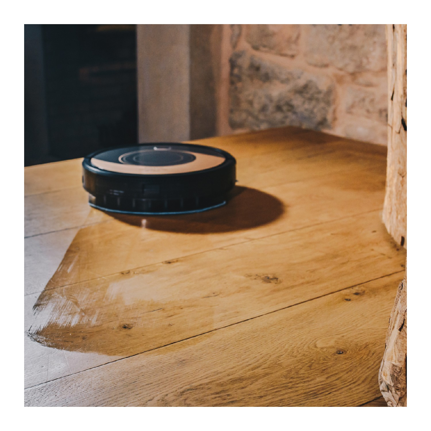 Una aspiradora robot negra y dorada sobre una mesa de madera. Reflejos de luz en la mesa.