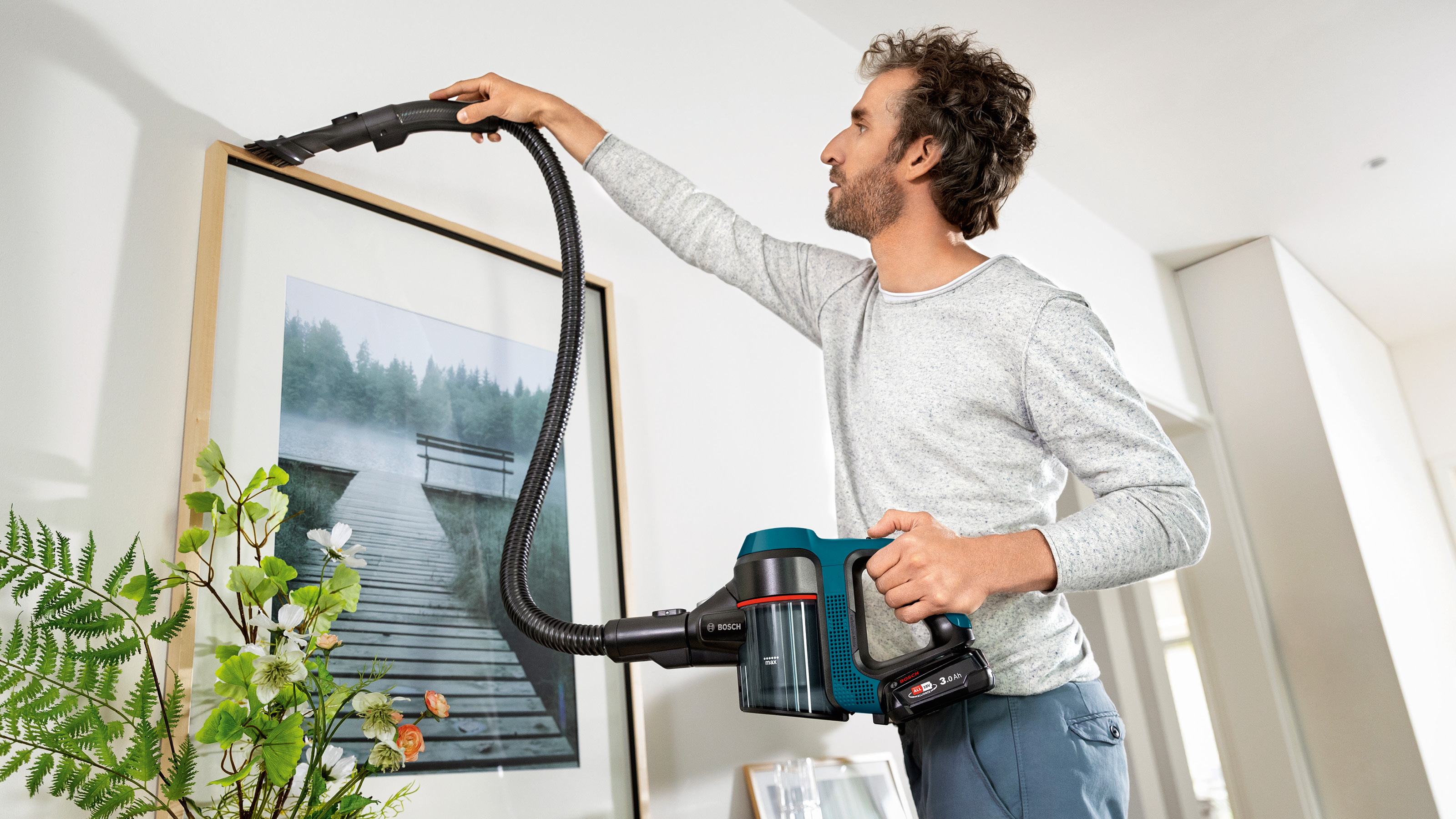 Ein Mann saugt eine Wand, mit einem Handstaubsauger. Ein Gemälde befindet sich an der Wand.
