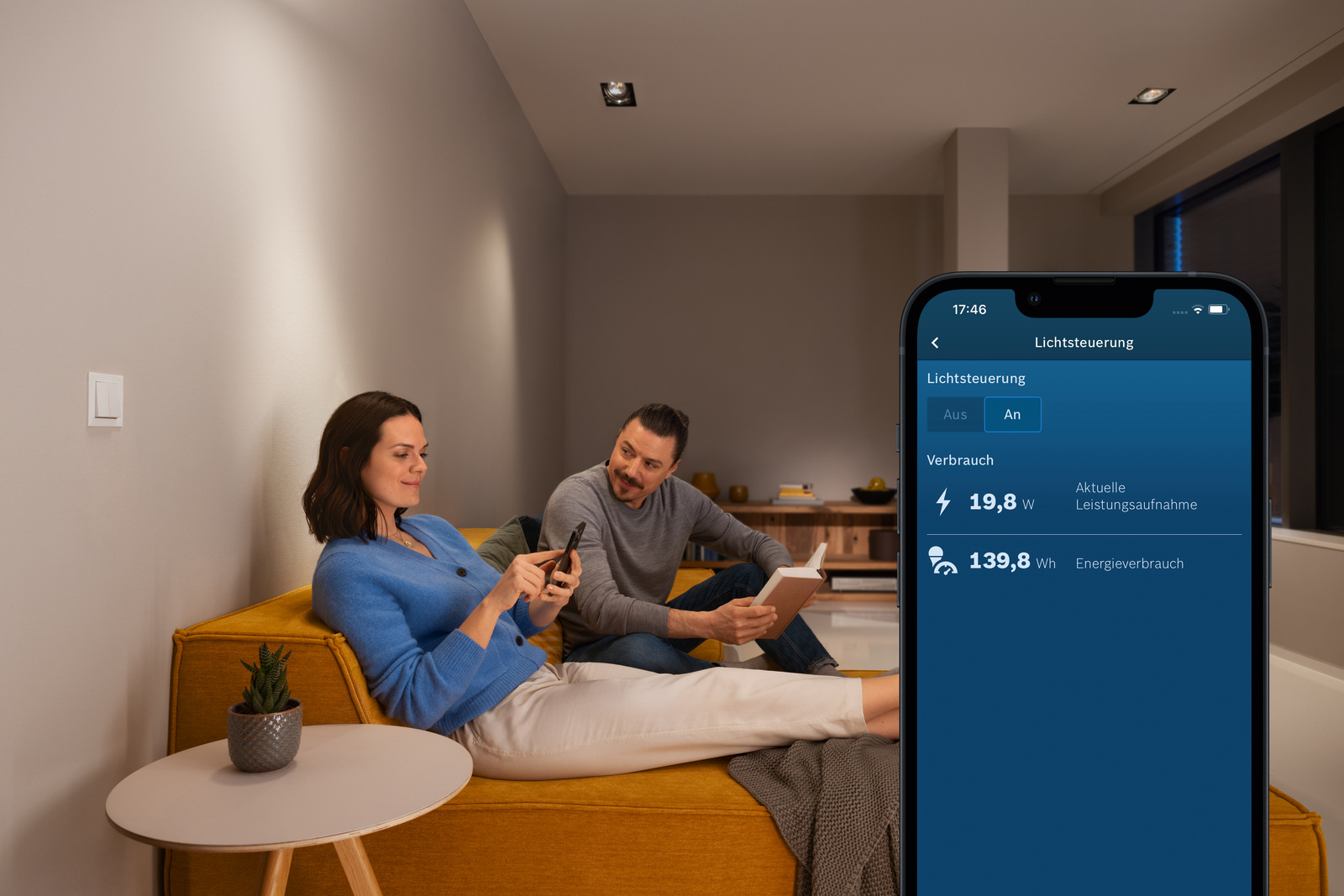 Ein Paar auf dem Sofa, das ein Smartphone benutzt, Fernsehbildschirm zeigt Stromverbrauch.