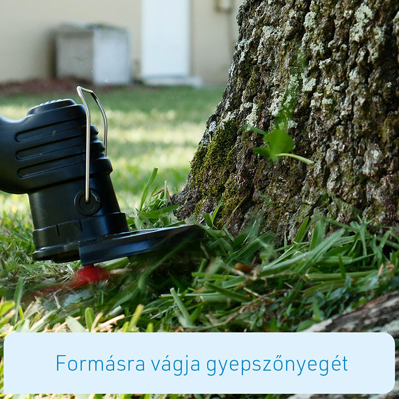 Személy fűnyíróval füvet nyír a fatörzs közelében, zöld fű és ház.