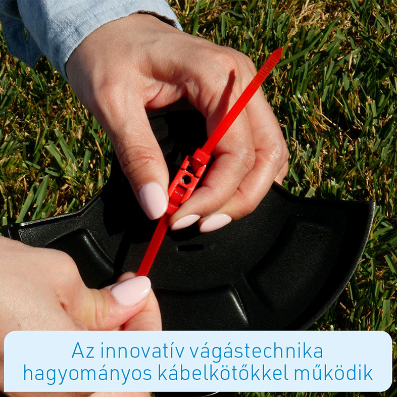 Kézben egy piros kábelkötegelő és egy fekete tárgy zöld fű háttér előtt.