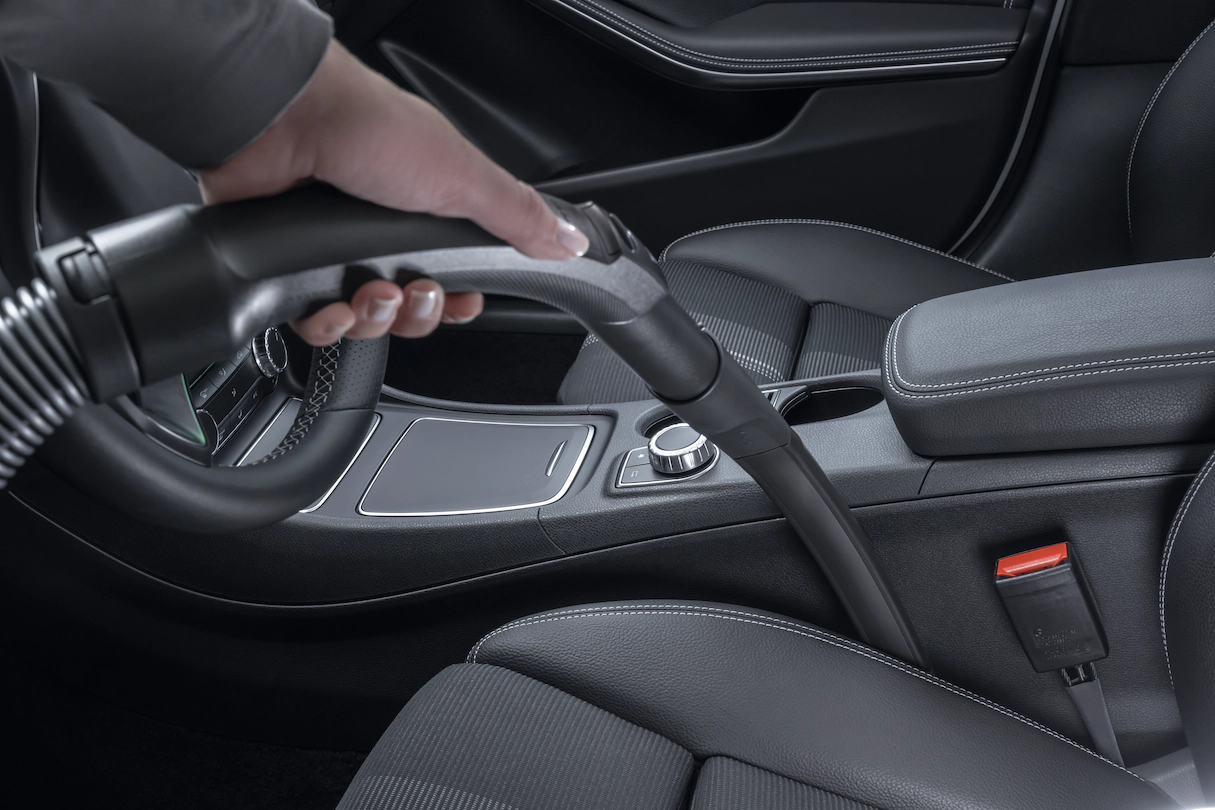 Hand stofzuigt een autostoel. Zwart interieur, focus op de schoonmaakactie.