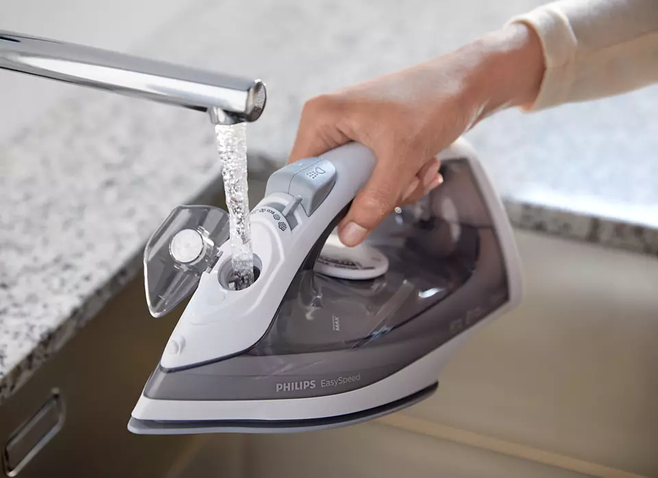 Une main remplit un fer à repasser Philips avec de l'eau d'un robinet, à côté d'un comptoir en granit.