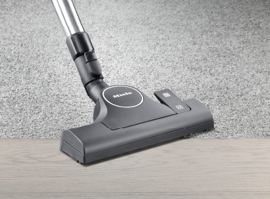 Tête d'aspirateur sur un sol en bois clair et un tapis gris.