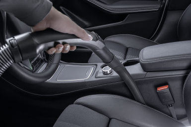 Une main aspirant un siège de voiture avec un aspirateur noir.