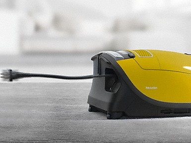 Un aspirateur jaune avec un cordon noir sur une surface grise.