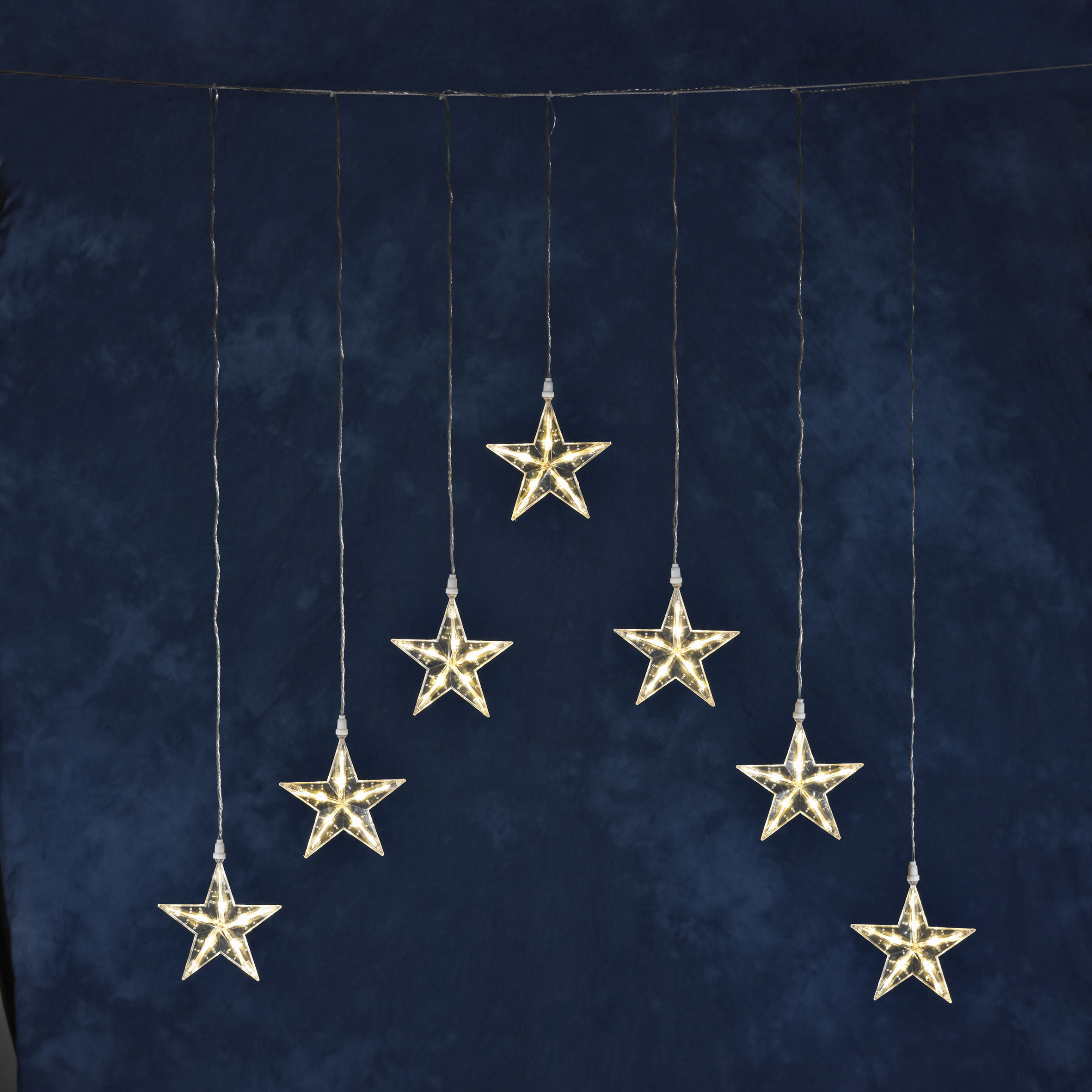 Sternförmige Lichter hängen an Schnüren vor dunklem blauem Hintergrund.