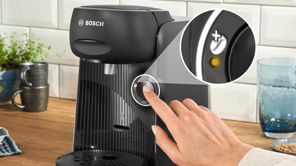 Eine Hand drückt eine Taste auf einer schwarz-grauen Kaffeemaschine. Nahaufnahme.