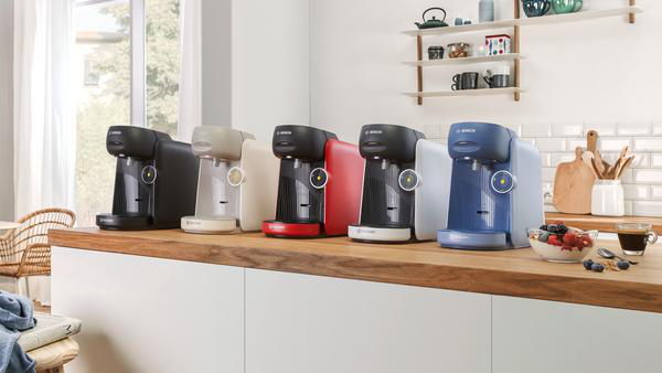 Mehrere Kaffeemaschinen in verschiedenen Farben auf einer Holztheke in einer Küche.