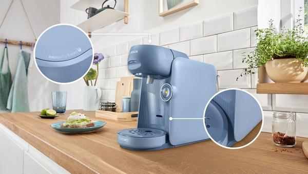 Eine blaue Kaffeemaschine auf einer Holz-Arbeitsplatte, mit einem Teller Essen und Blumen.