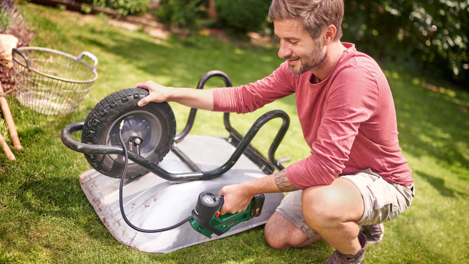 Egy férfi egy elektromos pumpával fújja fel a talicska kerekét egy kertben.