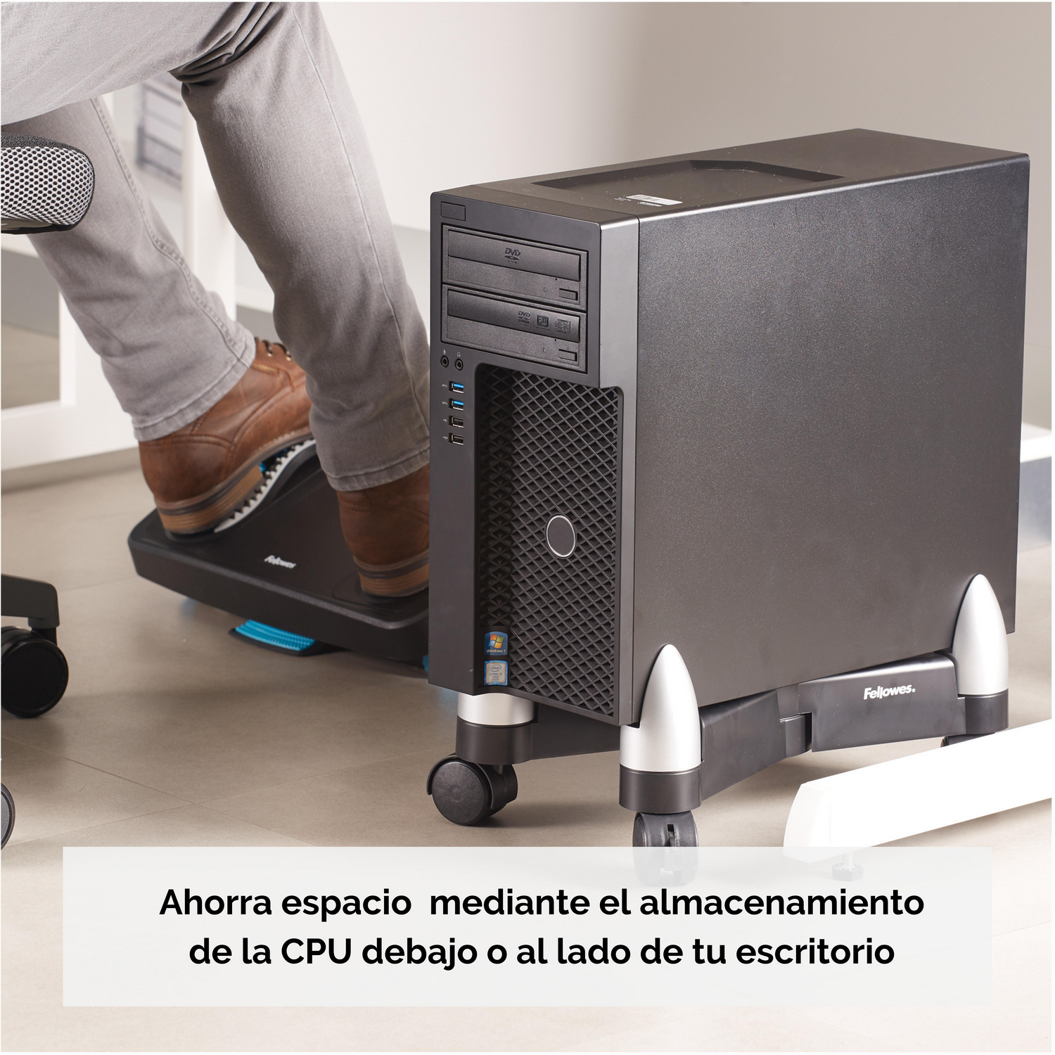 Piernas con zapatos marrones sobre un reposapiés ergonómico, junto a una torre de ordenador negra.