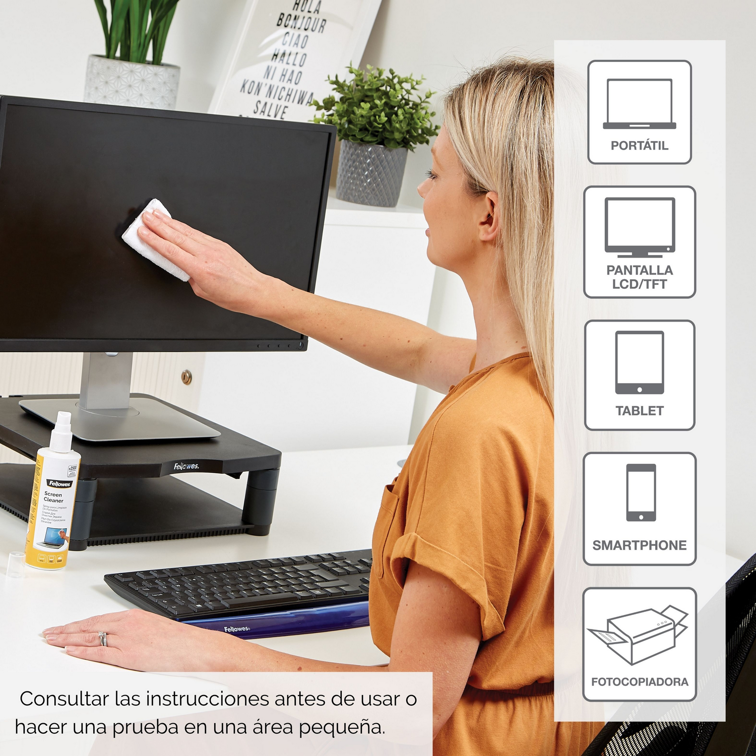 Una mujer limpiando un monitor con un pulverizador e iconos, sobre un escritorio blanco.