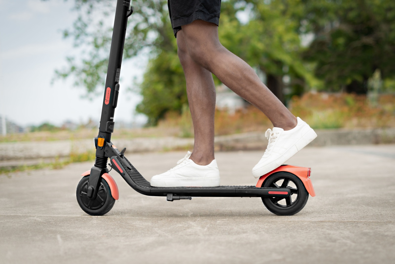 Bir kişi, gri bir yolda siyah ve mercan rengi bir scooter kullanıyor.